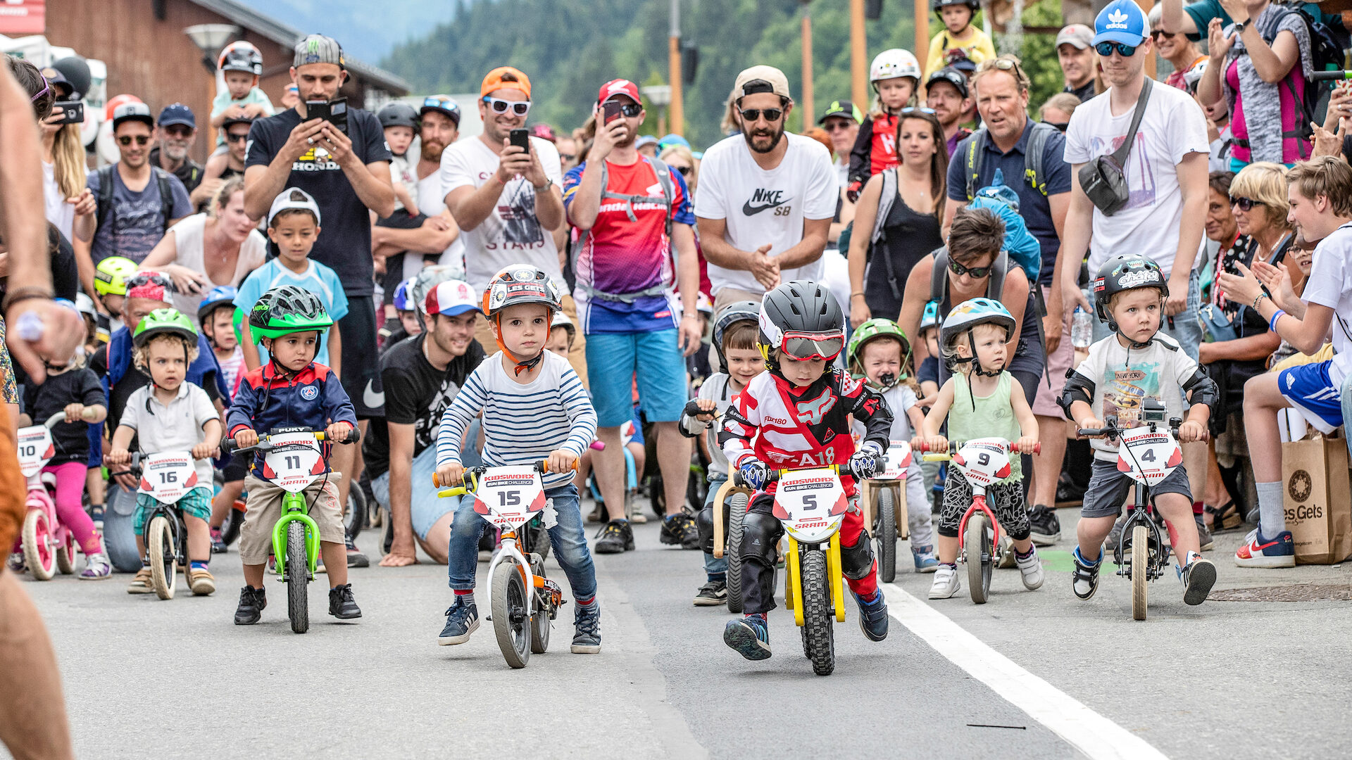 Petits enfants faisant une course de vélo avec parents les encourageant derrière