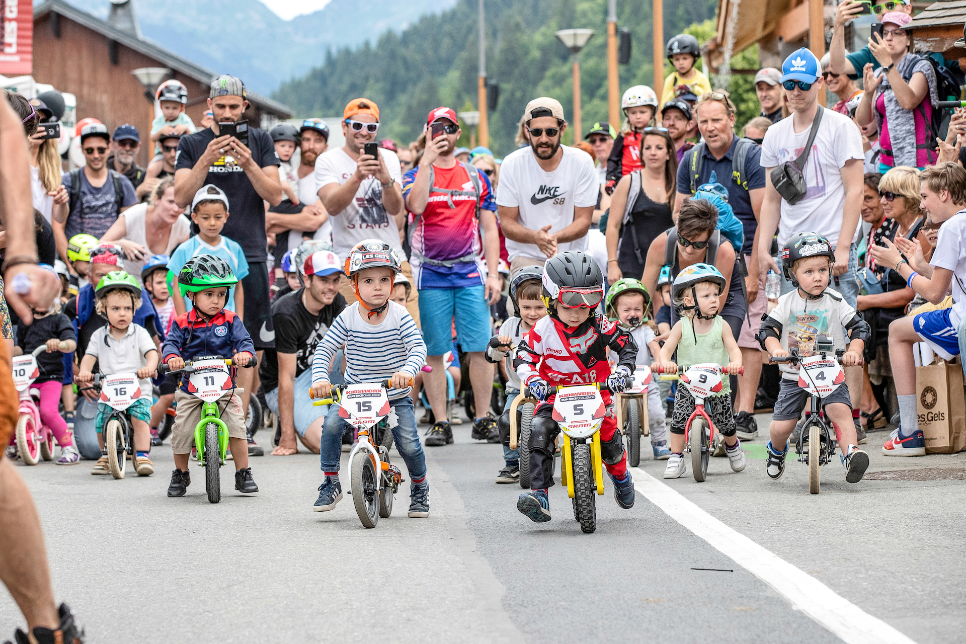 Petits enfants faisant une course de vélo avec parents les encourageant derrière