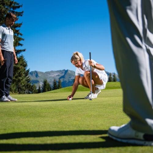 Three people playing golf with a woman putting the ball down.