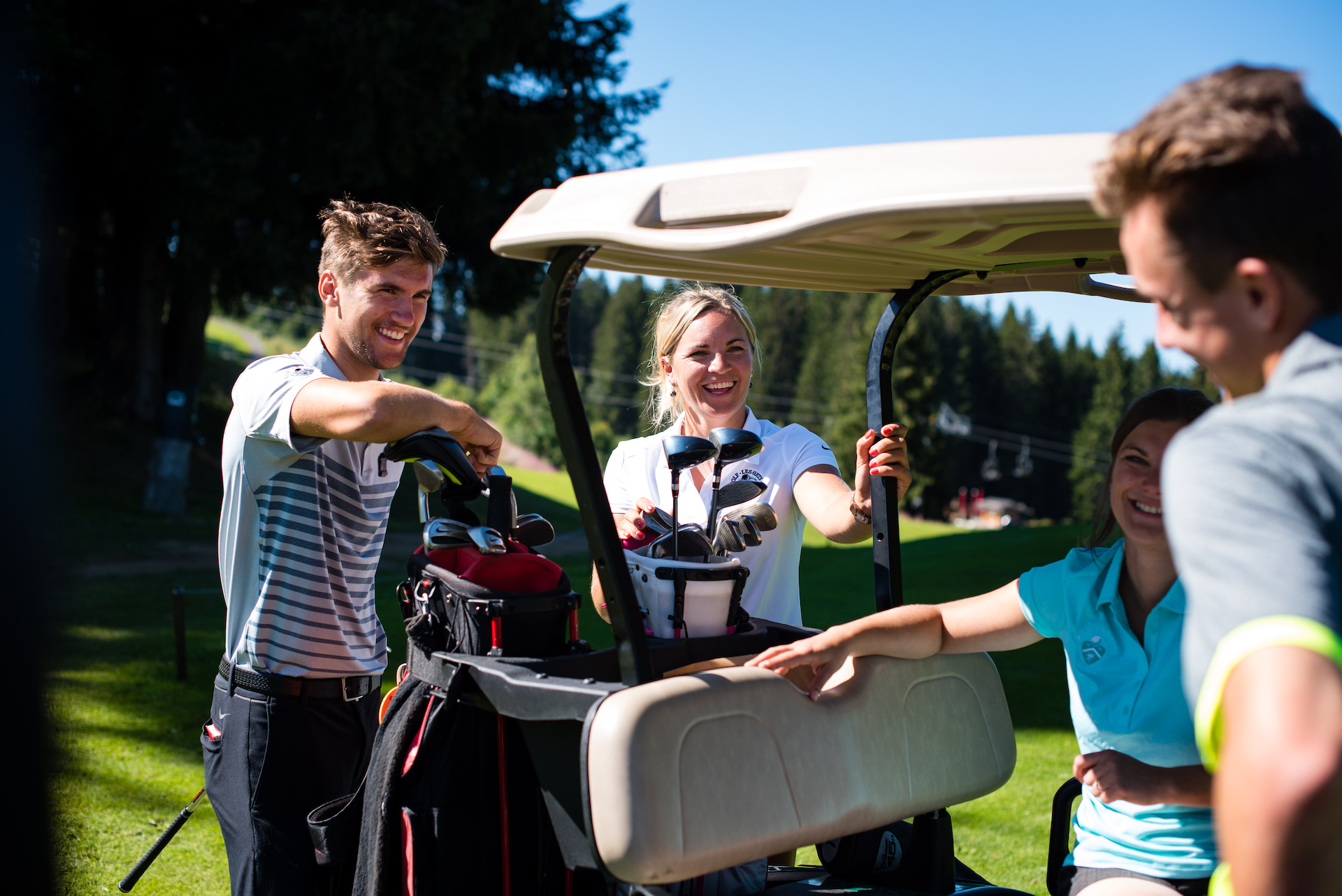 Groupe d'amis parlant et souriant à côté d'une voiturette de golf avec leur matériel