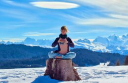 Femme faisant du yoga en hiver assise sur un tronc d'arbre avec montagne derrière