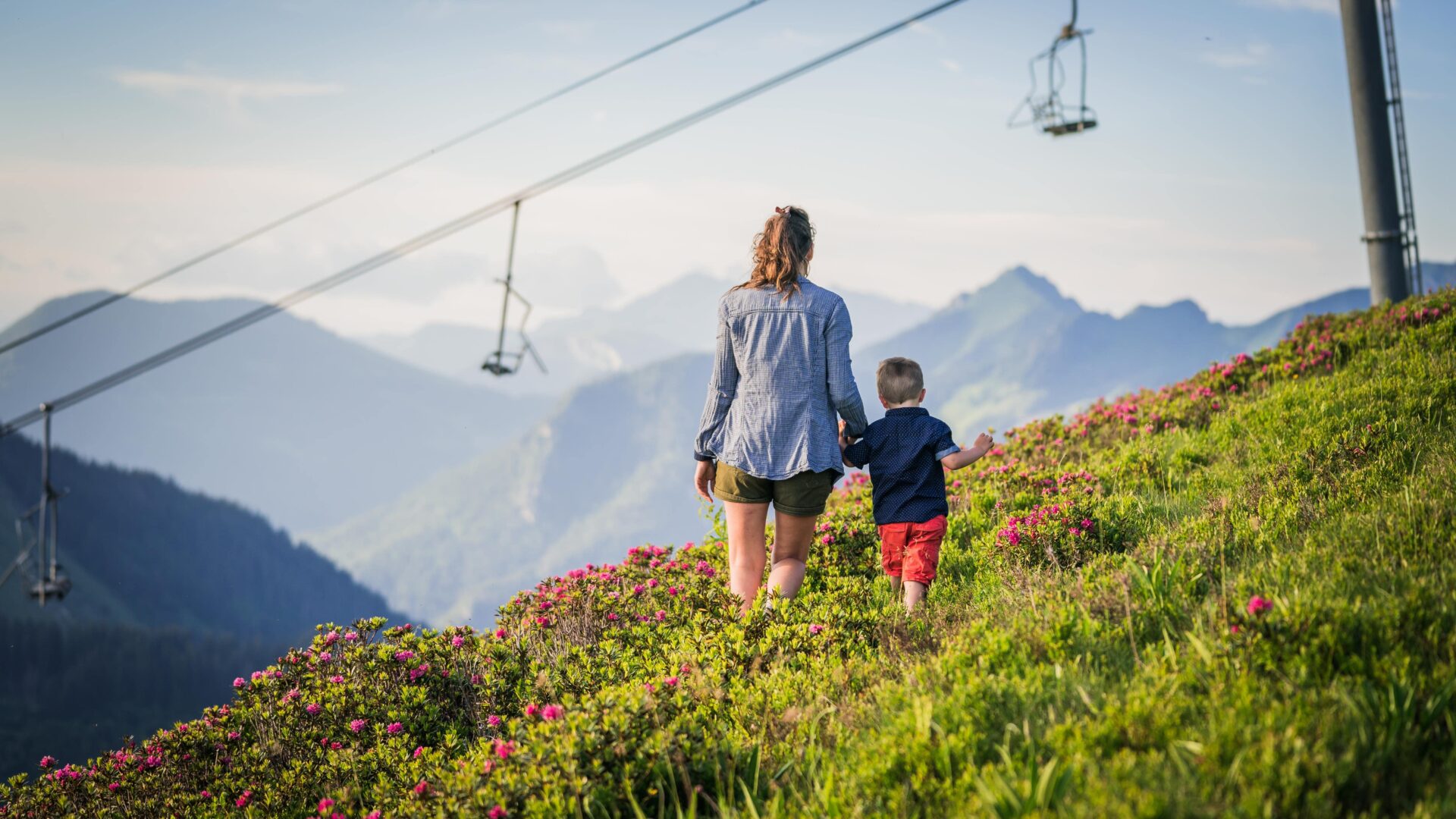 Femme et son fils se promenant en été en montagne avec télésièges derrière