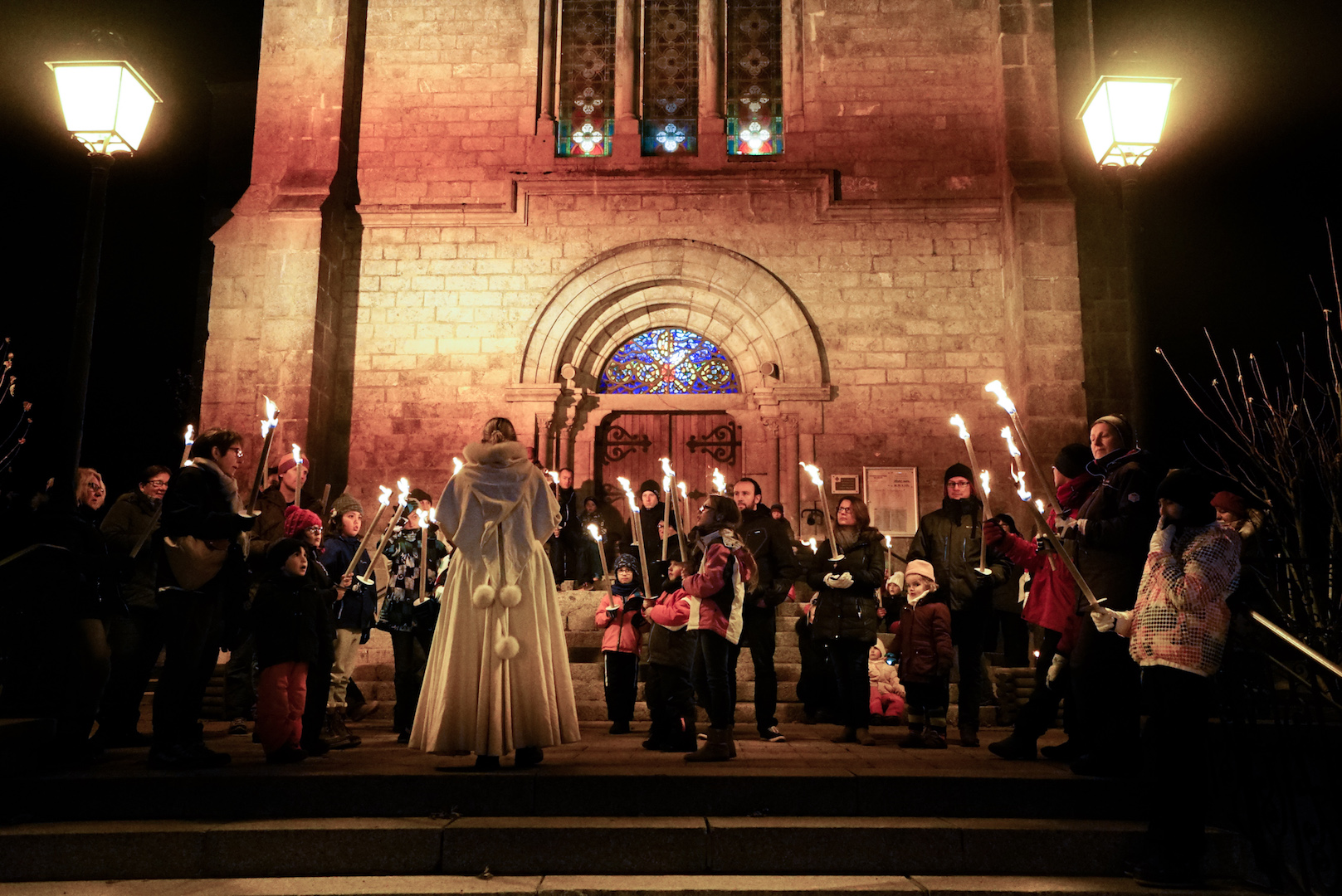 Groupe de personnes avec des flambeaux devant l'église pour l'animation balade contée