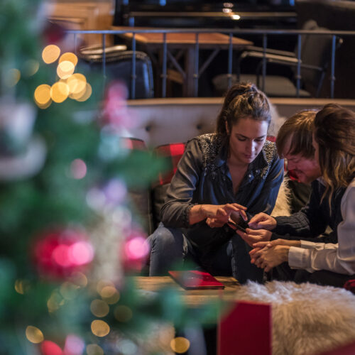 Amis assis dans un restaurant décoré pour noel et regardant leur téléphone